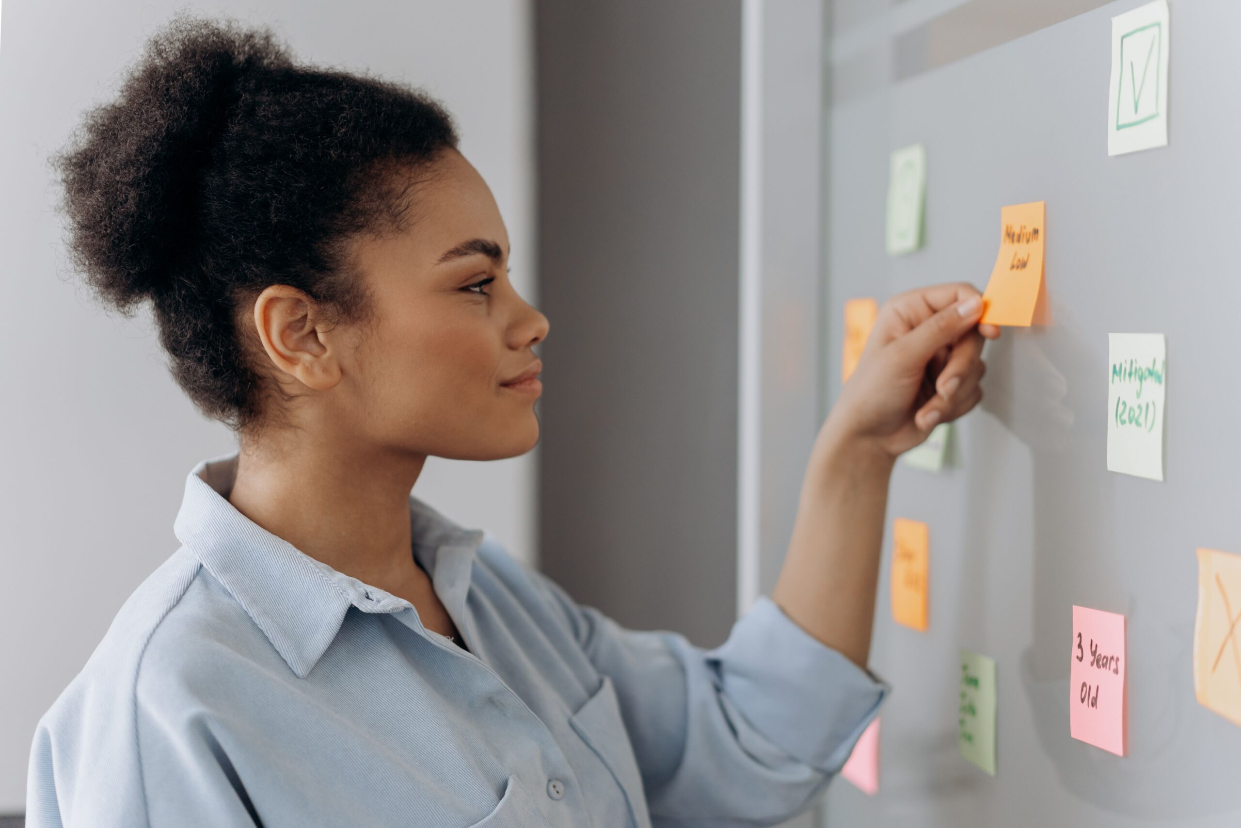 A professional woman organizing colorful sticky notes on a glass planning board, representing the process of mapping transferable skills to project management.