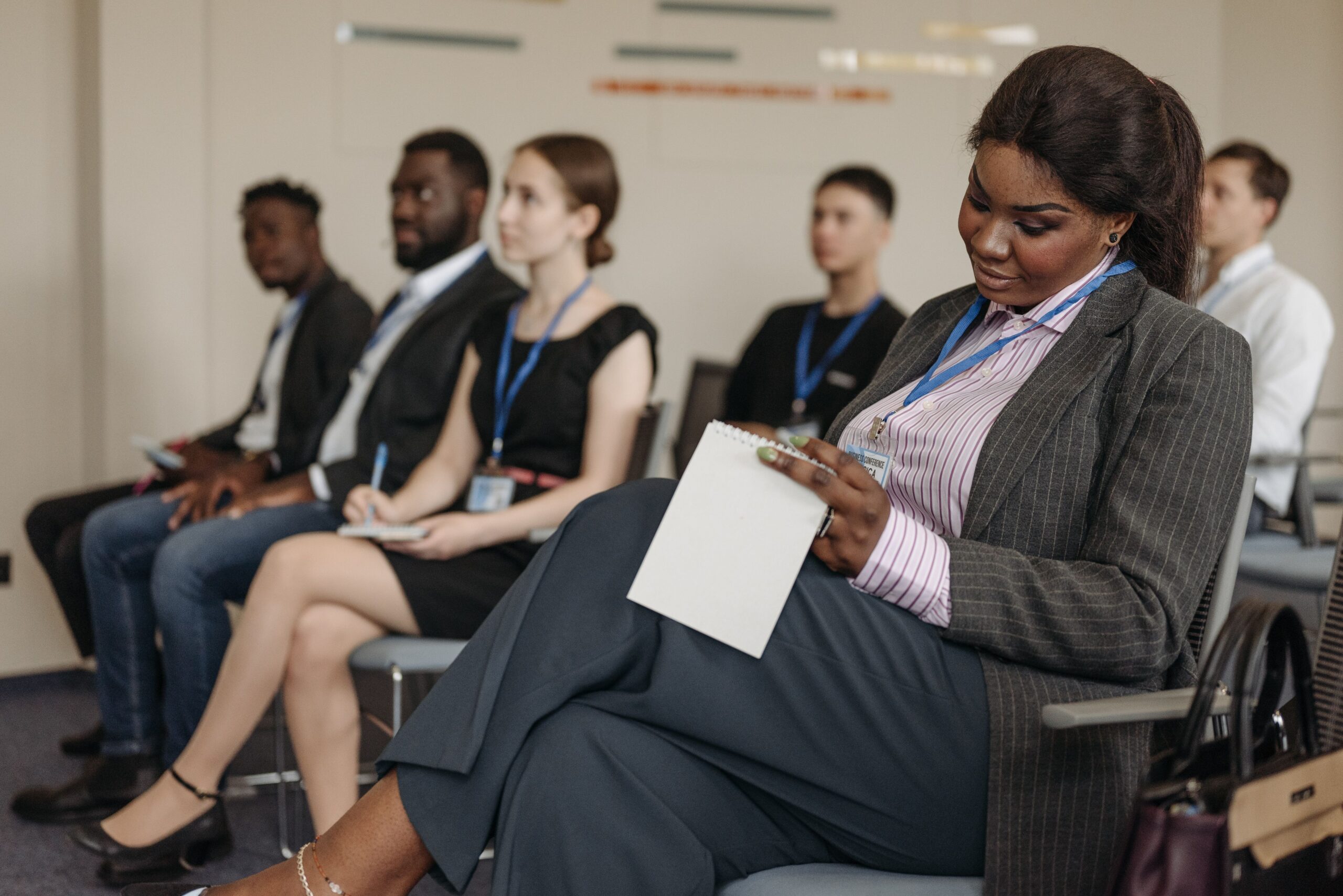 A focused Black woman in a business suit taking notes during UK project management training, representing professional development and bridging experience gaps.